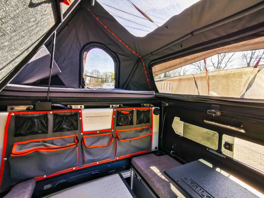 Vue depuis l'arrière du véhicule avec l'espace d evie et le couchage accessible une fois les trappes d'accès relevées